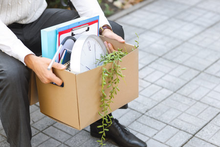 Fired male office worker with personal stuff sitting on bench outdoors, closeupの写真素材