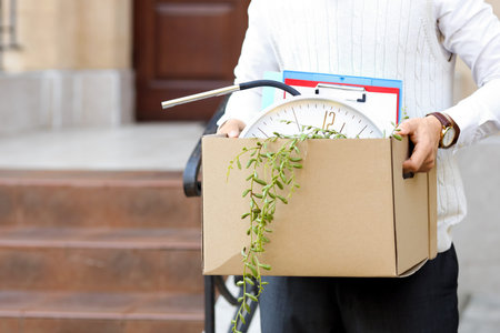 Fired male office worker holding box with personal stuff on street