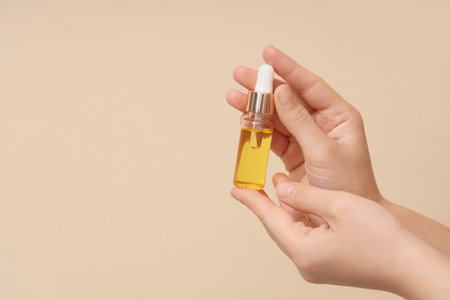 Female hands with bottle of essential oil on beige backgroundの写真素材