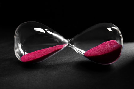 Hourglass with pink crystals on black background. Time management conceptの写真素材