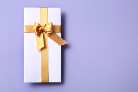 Paper card with bow made of golden satin ribbons on purple backgroundの写真素材