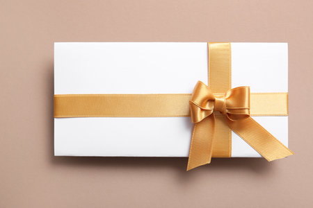 Paper card with bow made of golden satin ribbons on brown backgroundの写真素材