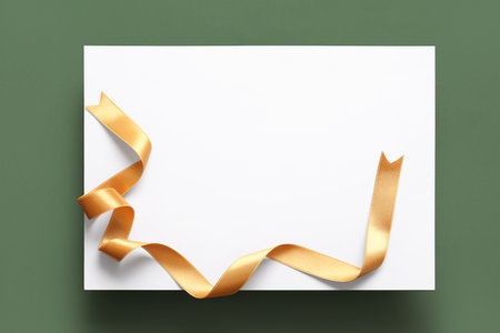 Blank paper sheet with golden satin ribbon on green backgroundの写真素材
