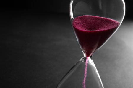 Hourglass with pink crystals on black background, closeup. Time management conceptの写真素材