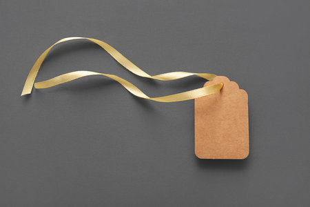 Blank paper tag with golden ribbon on gray backgroundの写真素材