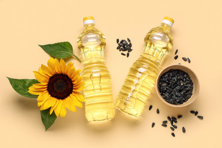 Bottles of oil, sunflower and bowl with seeds on beige backgroundの写真素材