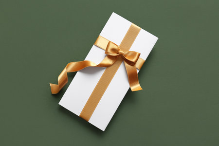 Paper card with bow made of golden ribbons on green backgroundの写真素材