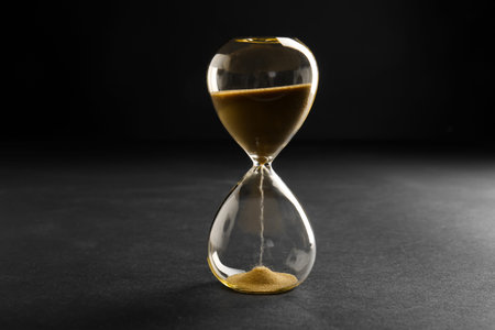 Hourglass with yellow crystals on black background. Time management concept