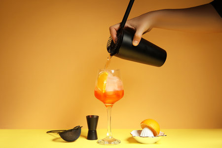 Female bartender making cocktail on yellow backgroundの写真素材