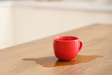 Red cup and spilled coffee on table in kitchen, closeupの写真素材