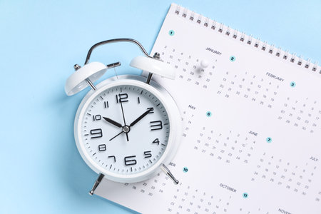 Calendar with alarm clock and paper pin on blue backgroundの写真素材