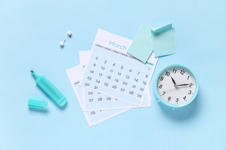 Calendar with alarm clock, sticky notes, marker and paper pins on blue backgroundの写真素材