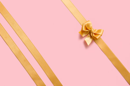 Bow made of golden satin ribbons on pink backgroundの写真素材