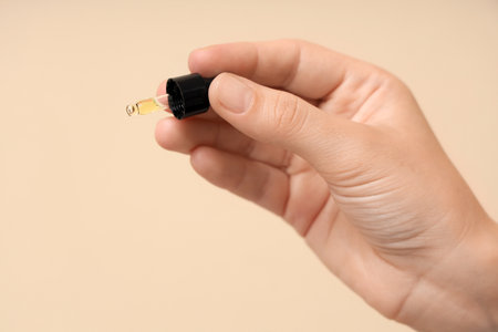 Female hand with essential oil on beige background, closeupの写真素材