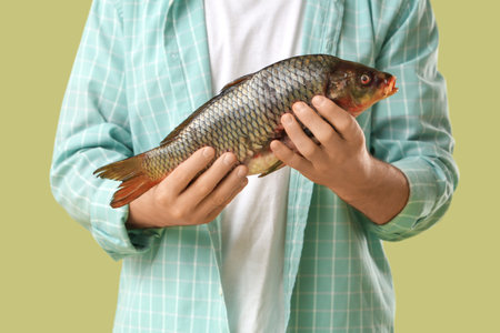 Young man with caught fish on green background, closeup