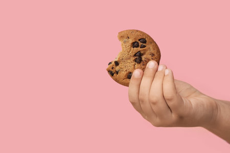 Little girl's hand with tasty cookie on pink backgroundの写真素材