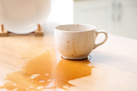 Cup and spilled coffee on table in kitchenの写真素材