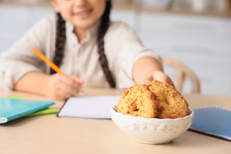 Little girl with tasty cookies doing homework at table in kitchen, closeupの写真素材