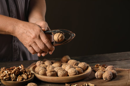Elderly woman cracking walnuts with nutcracker at wooden tableの写真素材