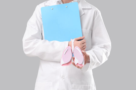 Female doctor with paper lungs and clipboard on gray background, closeupの写真素材