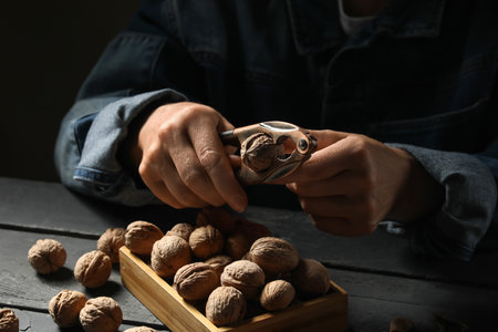 Elderly woman cracking walnuts with nutcracker on black wooden tableの写真素材