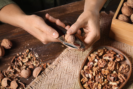 Woman cracking walnuts with nutcracker on wooden tableの写真素材