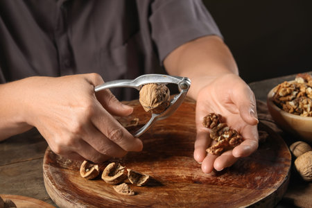 Elderly woman cracking walnuts with nutcracker on wooden table