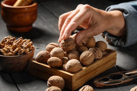 Female hand with walnuts and nutcracker on black wooden background