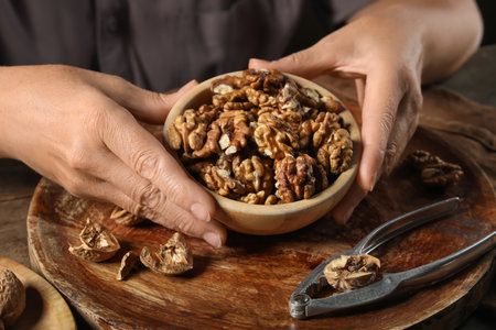 Elderly woman holding bowl with shelled walnuts on wooden tableの写真素材