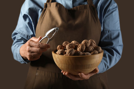 Elderly woman holding bowl of walnuts and nutcracker on brown backgroundの写真素材