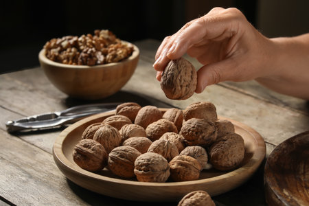 Elderly woman putting walnuts into bowl on wooden tableの写真素材