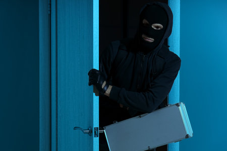 Male thief with case breaking through door of house at nightの写真素材