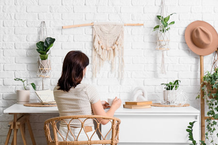 Young woman with coffee cup and houseplants at desk in office, back viewの写真素材