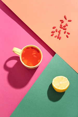 Cup of hot goji tea with lemon and berries on colorful backgroundの写真素材