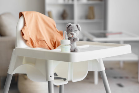 Baby highchair with bottle of milk and toy in living room, closeupの写真素材