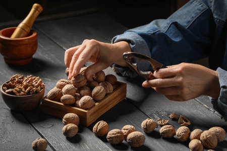 Elderly woman cracking walnuts with nutcracker on black wooden tableの写真素材