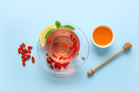Glass cup of hot goji tea with mint and bowl of honey on blue backgroundの写真素材