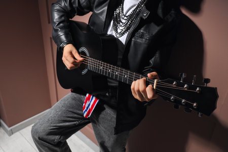 Young man in leather jacket playing guitar on brown backgroundの写真素材