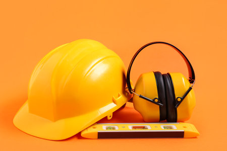 Yellow hardhat with hearing protectors and spirit level on orange backgroundの写真素材