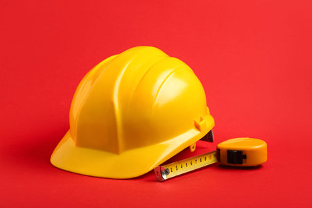 Yellow hardhat with measuring tape on red background