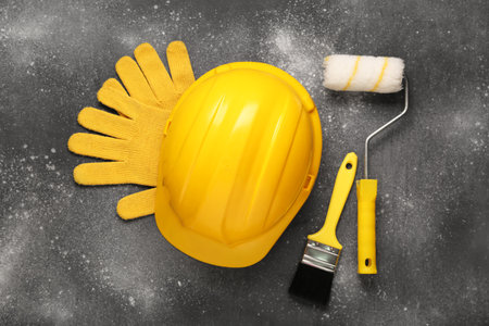 Yellow hardhat with gloves, paint roller and brush on gray grunge backgroundの写真素材