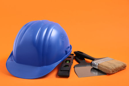 Blue hardhat with brush, trowel and spirit level on orange background