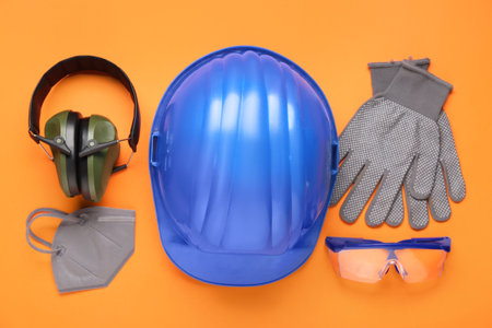 Hardhat, protective earmuffs and safety equipment on orange backgroundの写真素材