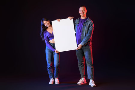 Young couple with big blank banner on black background