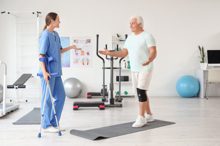 Senior man exercising without crutches and therapist in rehabilitation centerの写真素材