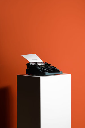 Vintage typewriter on pedestal against orange background