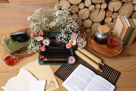 Vintage typewriter with flowers, tea and books on table near wooden wallの写真素材