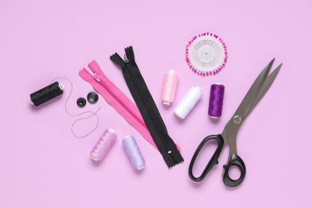 Thread spools with scissors, zippers and sewing pins on lilac backgroundの写真素材