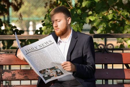 Young businessman reading newspaper on bench in parkの写真素材