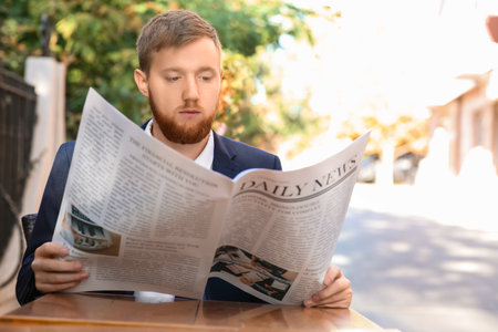 Young businessman reading newspaper in outdoor cafeの写真素材